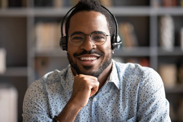 Smiling african professional telemarketer call center operator wear wireless headset look at camera, afro american business man customer technical customer support service closeup headshot portrait